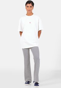 Witte oversized t-shirt met korte mouwen, rode geborduurde details. Gestreepte flared broeken in marineblauw en wit. Casual blauwe sneakers.