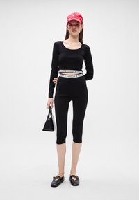 Crni dugi rukav s okruglim izrezom, crne uske tajice do članaka, bijela oznaka na pojasu, crvena kapa i crna torba.