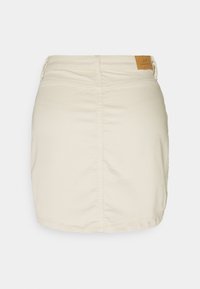 Beige Denim-Miniröcke mit geradem Schnitt, ausgestattet mit einem Aufnäher auf der Rückseite und einem seitlichen Reißverschlussdetail. Glatte Textur mit minimaler Nahtführung.
