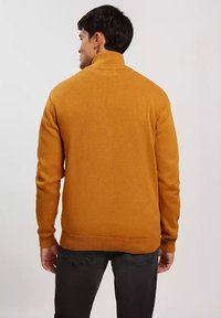 Musztardowy sweter dzianinowy z półgolfem i ściągaczami, charakteryzujący się teksturowanym materiałem i luźnym krojem.