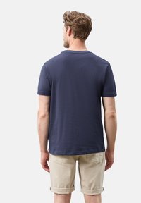 Granatowa bawełniana koszulka z okrągłym dekoltem i krótkimi rękawami, noszona z khaki szortami. Teksturowany materiał i luźny krój.