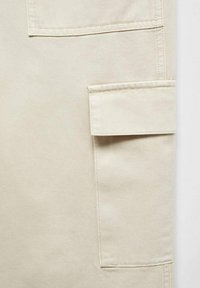 Beige cotton fabric with a textured weave, featuring a side patch pocket and reinforced stitching for durability.
