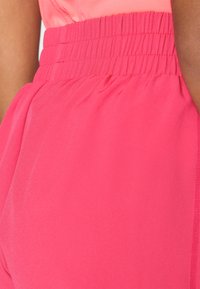 Cintura elástica rosa com textura franzida, combinada com um tecido fluido. O material parece leve e suave, criando um caimento suave.