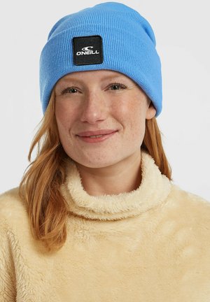 Blue knitted beanie with a black square label featuring the "Oneill" logo. The wearer has a light beige, textured fleece sweater.