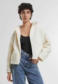 Fleece hoodie i cremet hvid med lynlås foran, oversized pasform, og to side lommer, parret med højtaljede blå jeans.