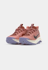 Baskets de sport roses avec un dessus en maille texturée, logo Nike noir et semelle extérieure violette. Présente un laçage proéminent et des poignées à l'arrière.
