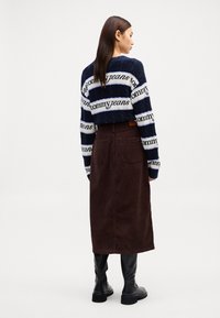 Pullover a righe navy e bianche in maglia con il testo "tommyjeans", abbinato a una gonna midi in velluto a coste marrone scuro e stivaletti neri.
