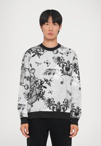 Μαύρο και λευκό πουλόβερ με σχέδια λουλουδιών και πεταλούδων, ριμπ μανίκια σε μαύρο χρώμα και στρογγυλή λαιμόκοψη σε ανοιχτό φόντο.