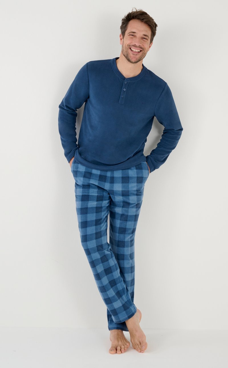 Blauwe langemouwen henley-shirt met drie knopen, gecombineerd met blauw en lichtblauw geruit pyjamabroek. Zachte stof, ontspannen pasvorm, blootsvoets.