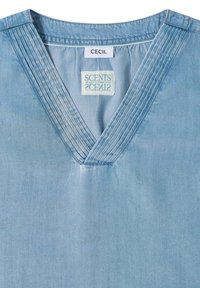 Chemise bleu clair à col en V avec des plis cousus verticalement le long du col et des étiquettes intérieures blanches portant les inscriptions "CECIL" et "SCENTS".