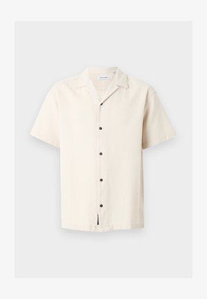 Chemise beige à manches courtes avec cinq boutons noirs et un col à pointes, présentée sur un fond gris clair.