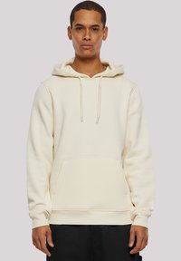 Sweatshirt à capuche couleur crème en tissu doux. Présente une poche kangourou à l'avant, des cordons de serrage et des bords côtelés aux manches et à l'ourlet.
