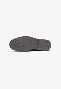 Suela de zapatilla negra con una superficie texturizada, forma redondeada y un ligero arco. El material parece goma con un acabado mate.