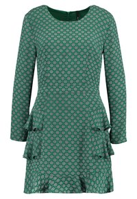 Vihreä mekko, jossa on pitkät hihat, pyöreä kaula-aukko ja liehuva helma, jossa on kaksi volaania. Kankaan kuvioinnissa on geometrinen muotoilu, jossa on valkoisia yksityiskohtia.