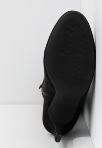 Stivale alla caviglia in suede nero con suola in gomma testurizzata. Presenta una chiusura con zip e una punta rotonda liscia. Dettagli laterali vicino alla zip.