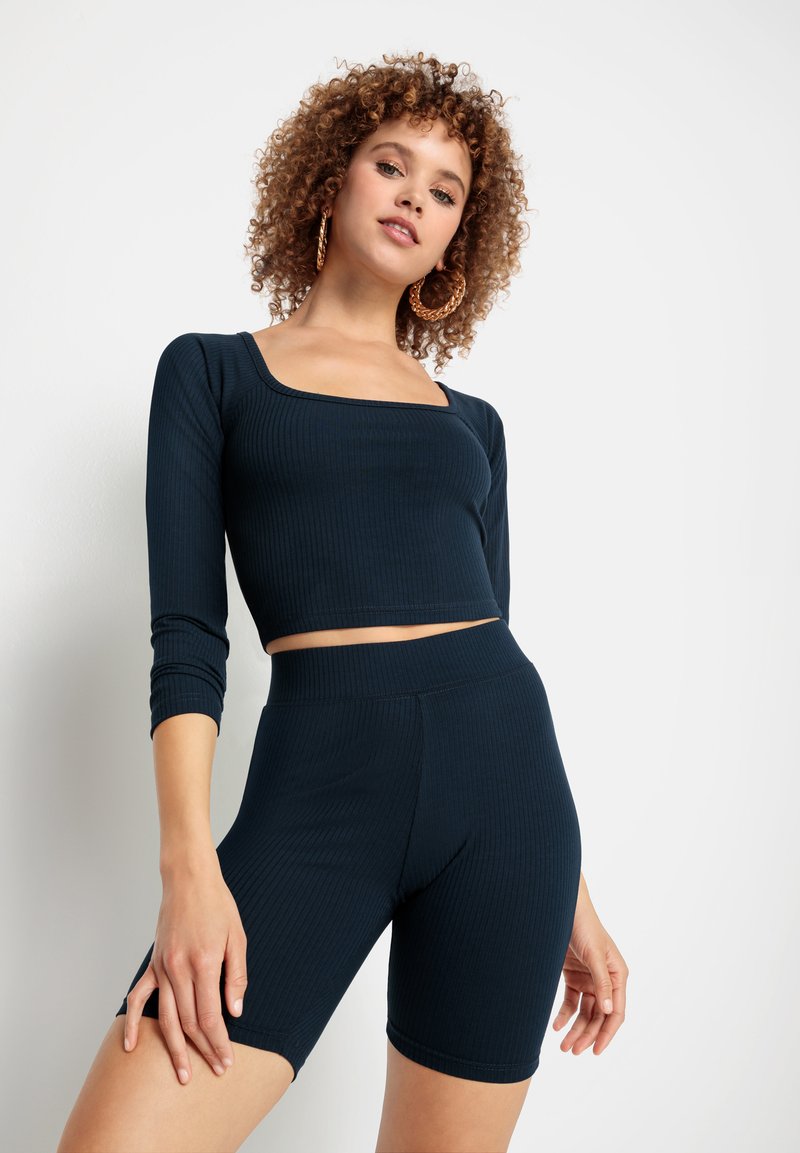 Granatowy prążkowany crop top z długimi rękawami i kwadratowym dekoltem, zestawiony z pasującymi szortami o wysokim stanie. Gładka tekstura, dopasowany krój.