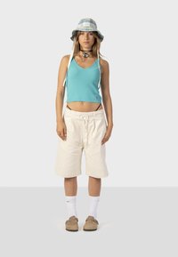 Svetlomodrý rebrovaný crop top, biele voľné šortky, béžové nazúvacie topánky, biele členkové ponožky a károvaný klobúk s bradou.