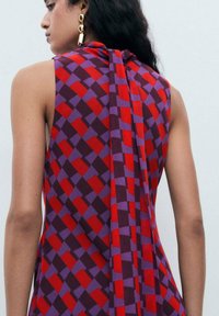 Ärmelloses Oberteil mit einem geometrischen karierten Muster in Rot, Lila und Dunkellila, mit einem drapierten Rückendetail. Glatte Stoffstruktur.