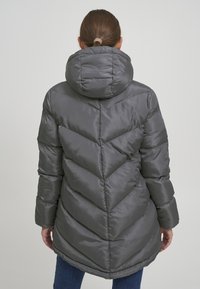 Grå pufferjakke med hette, med et chevron-quiltet design og en buet søm. Glatt, blankt stoff med lange ermer.