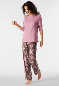 Top lungo a maniche corte di colore rosa chiaro con tasca, abbinato a pantaloni scuri con stampa floreale in rosa tenue. Realizzato in tessuto confortevole.