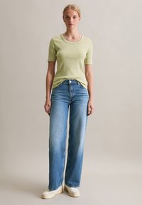 Lichtgroene geribde T-shirt met een ronde hals, gecombineerd met hoge, wijde blauwe jeans en crèmekleurige sneakers. Eenvoudig en casual ontwerp.