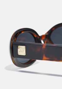 Tortoiseshell sunglasses with dark lenses, rounded frames, and a gold metal accent on the side. Smooth finish with a glossy texture.