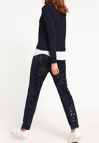 Navy långärmad topp med ett texturerat mönster, kombinerad med svarta byxor med paljetter och sidostrecker samt vita sneakers.