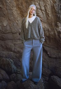 Szary, oversize sweter z dzianiny z dekoltem w serek, zestawiony z luźnymi szarymi spodenkami dresowymi. Strój charakteryzuje się miękką teksturą i luźnym krojem.