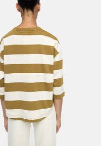 Oversize'owy top w paski w kolorze musztardowym i białym, wykonany z miękkiego materiału, z szerokim dekoltem i rękawami o długości trzech kwart.