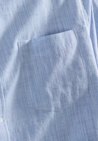 Hellblauses Hemd aus strukturiertem Stoff mit einer Brusttasche. Der Stoff zeigt dezente, vertikale Streifen und hat eine weiche Oberfläche.