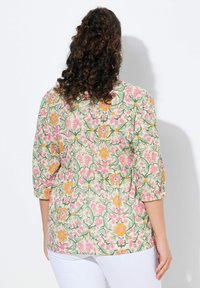 Blusa floreale in tonalità pastello chiare con motivi rosa, giallo e verde. Maniche a tre quarti e vestibilità comoda con dettagli arricciati.