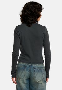 Dopasowany longsleeve w ciemnoszarym kolorze z bawełny, z okrągłym dekoltem i skróconym dołem, w zestawieniu z jasnoniebieskimi dżinsami z tylnymi kieszeniami.