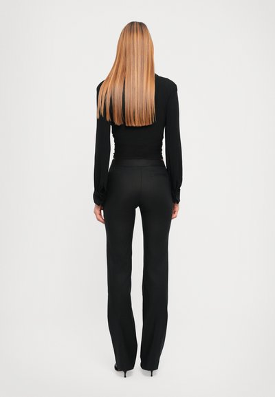 Haut à manches longues noir et pantalon noir ajusté. Le tissu semble lisse avec un léger éclat. Cheveux longs et raides, coiffés lâchement.