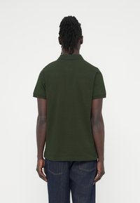 Σκούρο πράσινο πόλο μπλουζάκι με κοντά μανίκια, κλασικό γιακά και ελαφρώς υφασμένο ύφασμα. Η πίσω όψη δείχνει καθαρές γραμμές χωρίς ορατά λογότυπα.