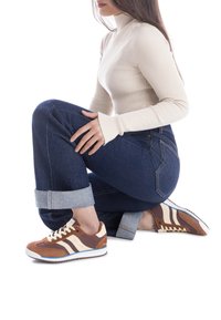 Zapatillas deportivas marrones y crema con materiales de ante y cuero, con un diseño de rayas, cordones y una suela de goma blanca.