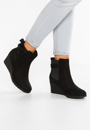 Bottines compensées noires avec panneaux latéraux élastiques portées avec un jean skinny gris clair aux deux pieds.