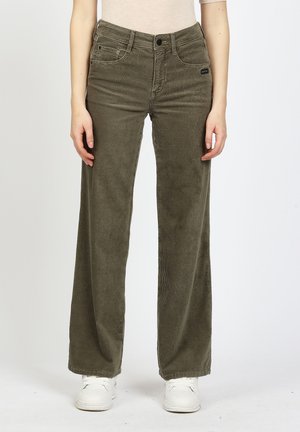 Person wearing olive green corduroy wide-leg pants and white sneakers, standing against a plain light background.