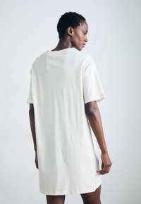 Loose-fitting cream cotton t-shirt dress with short sleeves, round neckline, and side slits, featuring a smooth texture and casual design.
