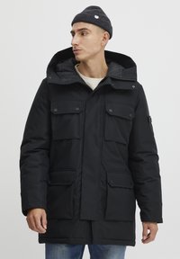 Sort parka-jakke med hætte, flere frontlommer, lynlås lukning og trykknapper. Designet med en flad, glat overflade.