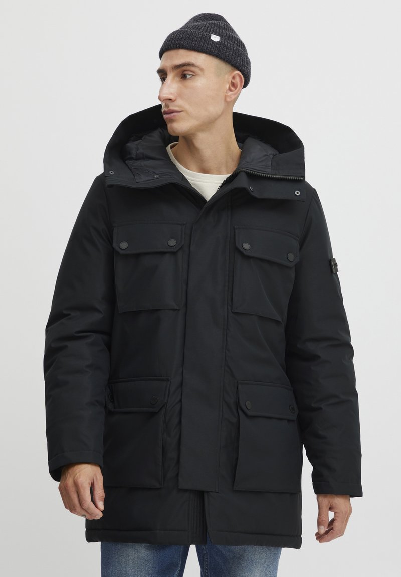 Sort parka-jakke med hætte, flere frontlommer, lynlås lukning og trykknapper. Designet med en flad, glat overflade.