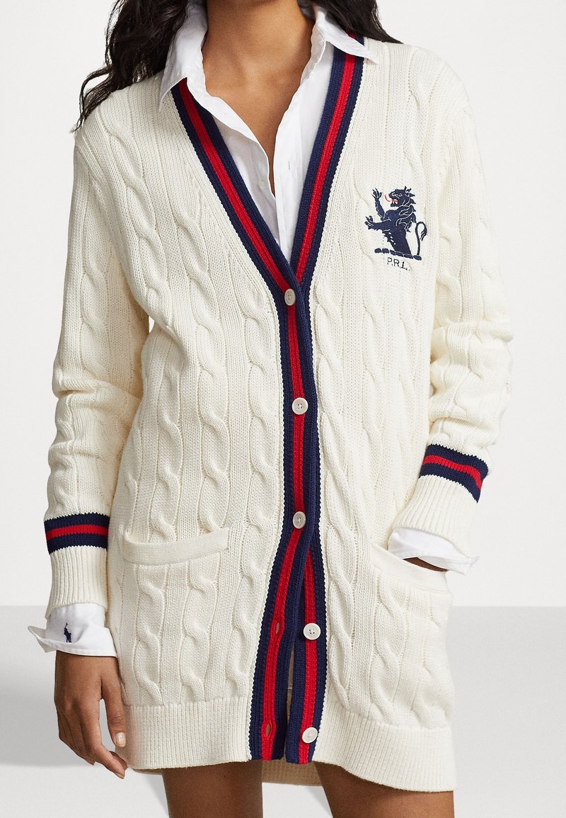 Vit kabelstickad cardigan med djup V-hals, röd och marinblå randig kant och logotypbroderi. Inkluderar framfickor och knappar.