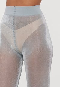 Leggings lucidi, di colore azzurro chiaro, a vita alta realizzati in materiale trasparente e metallico. Presentano una vita morbida e una finitura texturizzata.