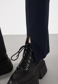 Navy ribbed pants with side slits, paired with black lace-up platform boots featuring prominent eyelets and a textured sole.