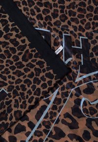 Tissu à imprimé léopard marron et noir plié avec une petite étiquette de marque blanche "Cecil" visible.
