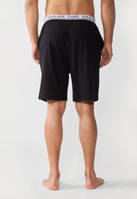 Svarte bomullsshorts med en komfortabel elastisk linning med hvit "PIER ONE" tekst. Glatt tekstur, knelange design, uten lommer.