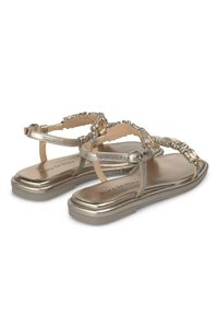 Sandales dorées métalliques avec des perles décoratives et une semelle plate. Équipées d'une bride ajustable à la cheville et d'une semelle intérieure rembourrée pour le confort.