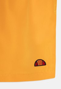 Rumena tkanina s prerezanim delom in gladko teksturo. Na robu se nahaja vezeno logo v mornarsko modri, oranžni in rdeči barvi.