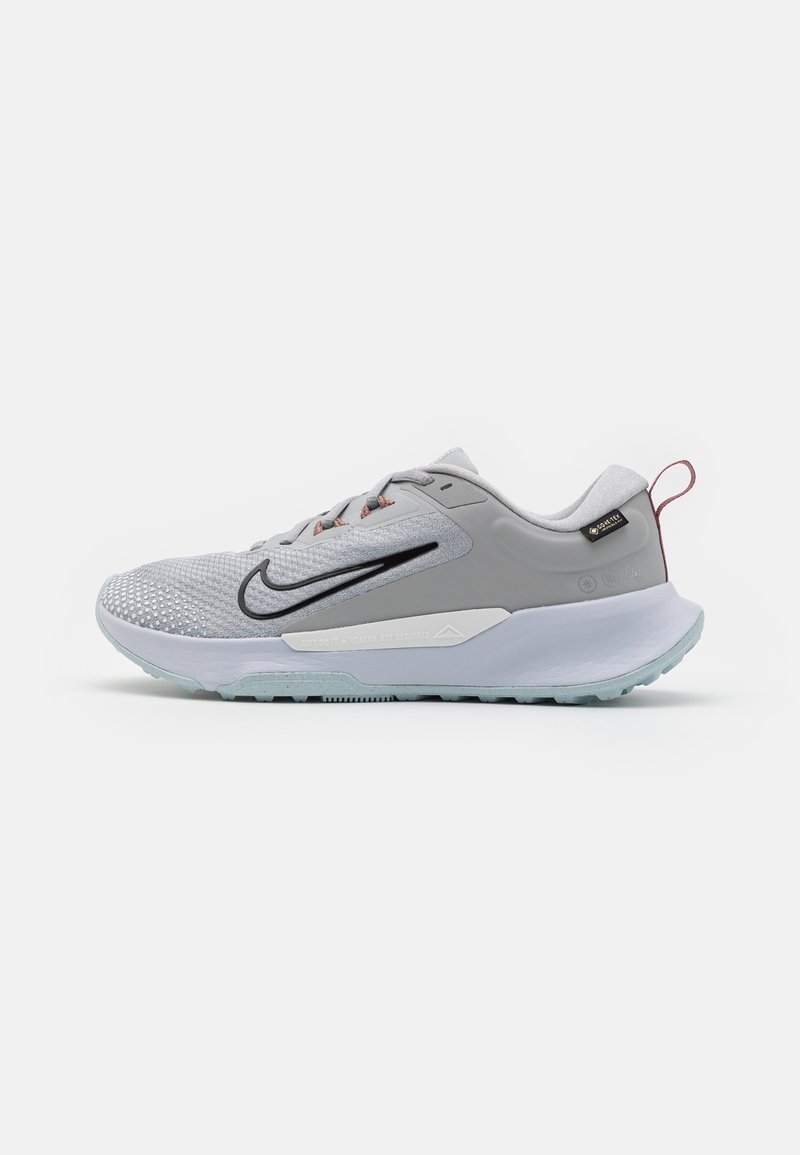 Chaussure de running Nike gris clair avec empeigne en mesh, logo swoosh noir, semelle blanche amortissante et languette rouge au talon.