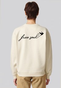 Felpa color crema con la scritta "free soul" ricamata in corsivo nero, accompagnata da una piccola grafica di un uccellino. Tessuto morbido e vestibilità rilassata.