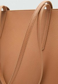 Tan leren draagtas met een textuur, voorzien van twee lange, gladde hengsels. Geen zichtbare hardware of extra accenten.